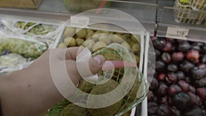 In grocery store someone`s hand gets small packed basket with kiwis.