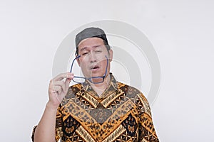 A groggy and stressed middle aged man takes off his glasses after feeling eyestrain. An overworked person wearing a batik shirt photo