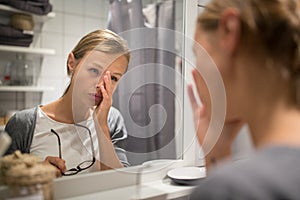 Groggy, young woman yawning in front of her bathroom mirror