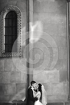 Grom huging kissing bride with red hair near wall outdoors Lviv photo