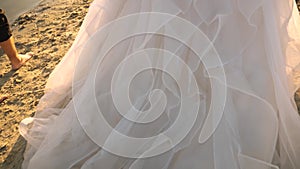 Groom barefoot and the bride in a white dress walk along the beach along the river. couple in love walks on the sand in