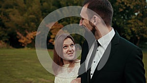 Groom with beard walks across lawn and talks to his bride smiling at each other.