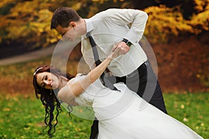 Groom bends bride over standing on the lawn in a park