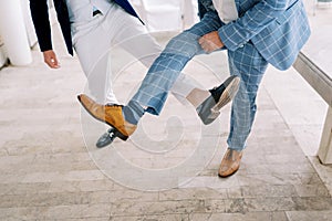 Groom and best man compete by showing their shoes on their outstretched legs. Cropped. Faceless