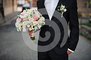 Groom in a black suit holding a gentle wedding bouquet