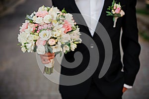 Groom in a black suit with boutonniere holding a wedding bouquet