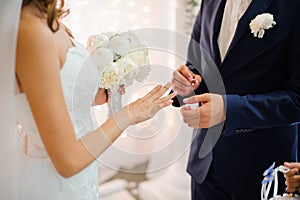 Groom puts on a gold wedding ring on the finger of a beautiful bride