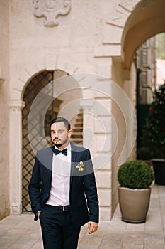 Groom in a blue suit walks through the courtyard of an old house with arches