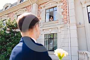 the groom with a bouquet of flowers is waiting for the bride on the window.