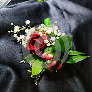 A groom boutonniere contains red rose, gyphsophilla, hypericum berry and caspea