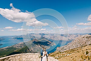 Groom and bride are embracing and looking at the Kotor Bay. Beautiful view from mountains of Montenegro