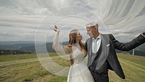 Groom with bride having fun on a mountain hills. Wedding couple under the veil. Happy family. Man and woman in love. Lovely groom