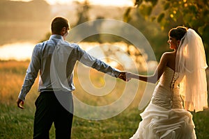 Groom and bride are holding hands on the background green forest
