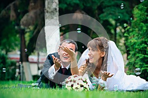 Groom and bride lie on a grass around soap bubbles