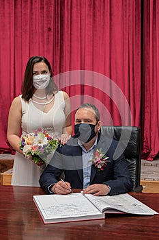 Groom and bride signing marriage contract in medical masks