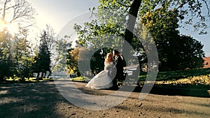 The groom and the bride are sitting on a park bench. Autumn Park and Morning Sun.