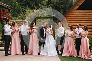 Groom and bride stand with groomsman and bridesmaid outside. Newlyweds kissing and friend clap. Wedding day photo