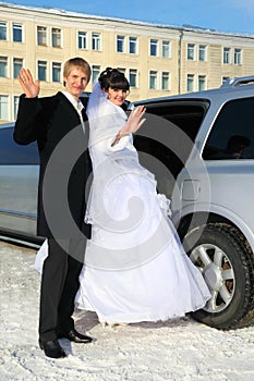 Groom and bride stand near wedding limousine