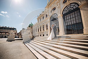 Groom and bride stand on stairs by the great palace in Wiena