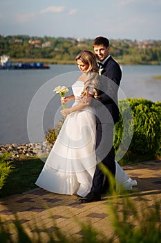 groom and bride in traditional wedding clothes cuddling in the park on the shore