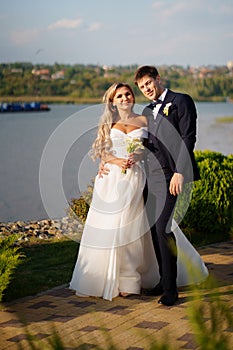 groom and bride in traditional wedding clothes cuddling in the park on the shore