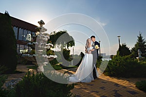 groom and bride in traditional wedding clothes cuddling in park. sunset