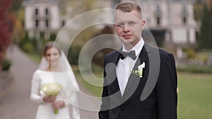 Groom and bride walking in the park by big palace. Handsome man and beautiful woman