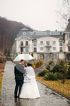 Groom and bride walking in the park on their wedding day. Autumn weather. Rair. Couple umbrella