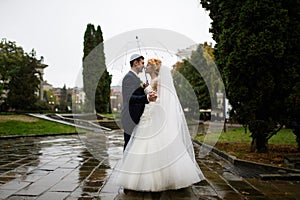 The groom and bride are walking under umbrella in the rain in the park