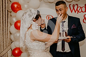 groom and bride at wedding cut their large multi-tiered white cake taste it fed from each other.