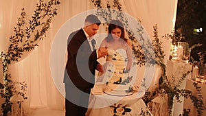 groom and bride at wedding cut their large multi-tiered white cake taste it fed from each other