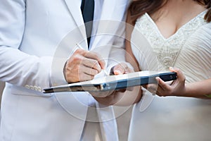 Groom and bride in white suit signing their marriage license