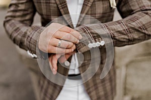 Groom in brown plaid jacket looks at his ring on the finger. Advert for wedding agency.