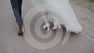 Groom in brown shoes and plaid trousers walks with bride along paving slabs