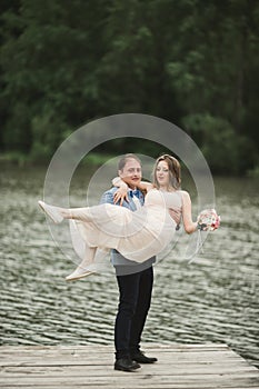 Groom carrying bride near lake and forest