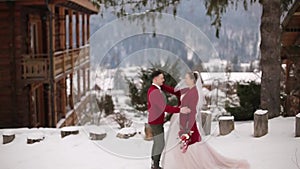 Groom comes to bride, hugs and kiss her in snowy mountain village at ski resort. Romantic wedding couple in knitted