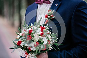 The groom in a dark blue jacket holds a bouquet of roses