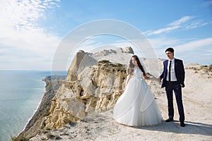 Groom in elegant suit and bride in white dress at weddingday on cliff with beautiful view of ocean photo