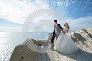 Groom in elegant suit and bride in white dress at weddingday on cliff with beautiful view of ocean photo