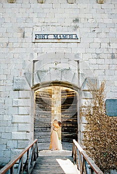 Groom embraces bride behind the ajar wooden door of Mamula Fort