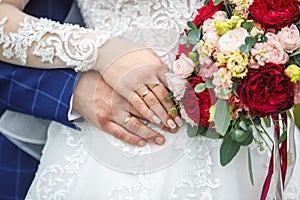 Groom embraces the bride with wedding red white rose bouquet. rings on the hands of newly-married couple