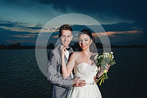 Groom embrecing bride on the river bank at night