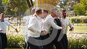Groom flexing and having fun walking with groomsmen on wedding day. Happy classy man in black suit, bow tie and