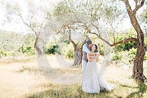 the groom gently hugs the bride from behind in the olive grove groom is kissing bride