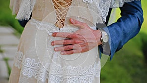 The groom gently puts his arm around the bride`s waist. The man`s hands on the girl`s waist