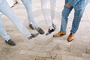 Groom and groomsmen show off their shoes with outstretched feet. Cropped. Faceless