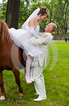 groom helps fiancee to get down from a horse