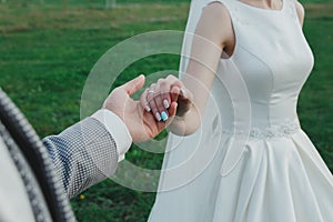 Groom is holding beautiful bride`s hand is standing outdoors. Wedding manicure nails in tiffany light blue color. Elegant satin