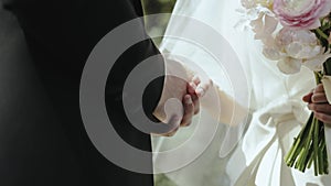 Groom holding brides hand on the ceremony. Bride hold bouquet of tender white and pink roses. Newlywed couple standing