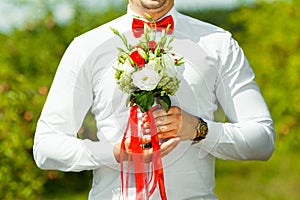 Groom holding in hands delicate, expensive, trendy bridal wedding bouquet of flowers in red and white